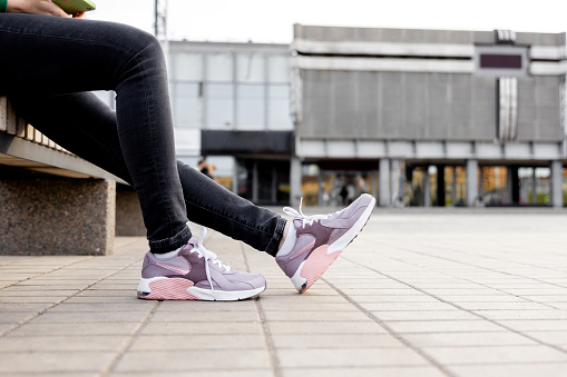woman in black jeans and sneakers sits on bench. Womens legs in pink sneakers close up