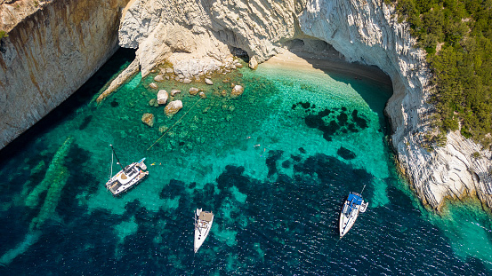 Beautiful wild coast with amazing remote beach and forest around on Mediterranean sea and one anchored sailboats in shallow water with crew enjoying in nature. Island of Kalamos, Greece.