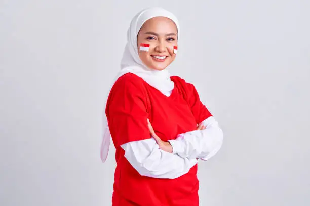 Smiling young Asian muslim woman in red white t-shirt crossed arms and looking confident celebrating indonesian independence day on 17 august isolated on background