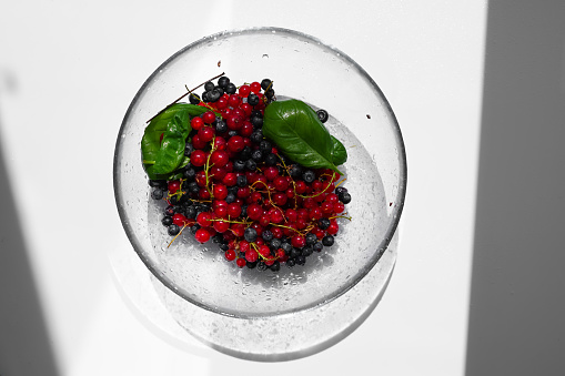 Transparent glass bowl with berries. Currants, blueberries and basil leaves are ready to eat raw