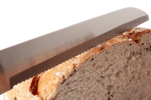 Slicing fresh bread by special knife close up. Serrated knife for bread blade.
