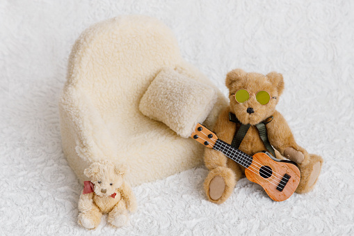 Shoot set up with sofa, teddy bear wearing sunglasses and guitar for newborn on white background. Photo zone for a photo session of newborns. Setup ready for newborn photo shoot and baby photography.
