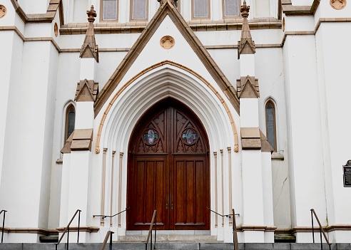 Cathedral front doors in Savannah, Georgia. Brown wooden doors and white building.