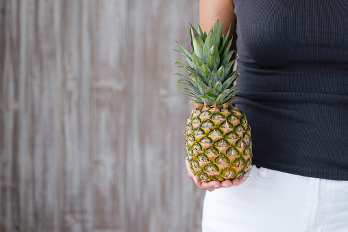 Unrecognizable female is holding pineapple in hand representing vegetarian and vegan food.