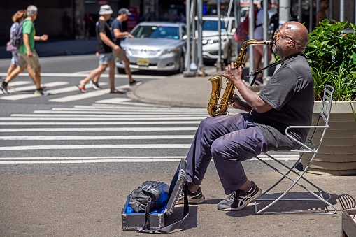 Times Square, New York, NY, USA - June 26, 2022: African American man playing a saxophone sitting on a chair at Broadway