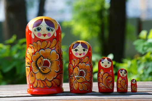 A row of nesting dolls in close-up against a background of green foliage. Slavic culture.
