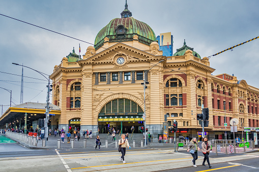 Pedestrians walk in front of Flinders Street Railway Station in Melbourne, Victoria, Australia on an overcast day.