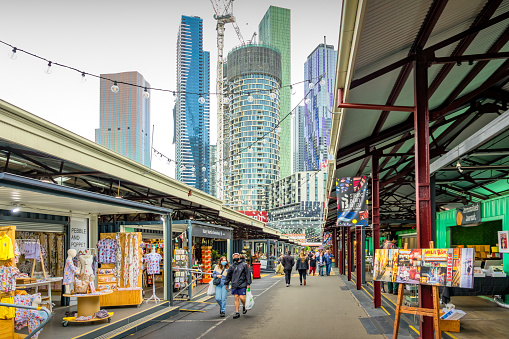 Pedestrians walk past stores at Queen Victoria Market in Melbourne, Victoria, Australia, with new condo towers in the background, on an overcast day.