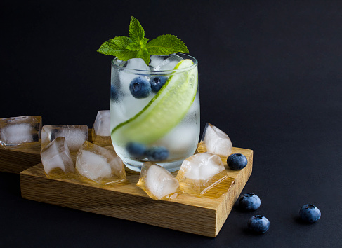 Summer drink with cucumber, mint and blueberry in the glass on the dark background. Copy space.