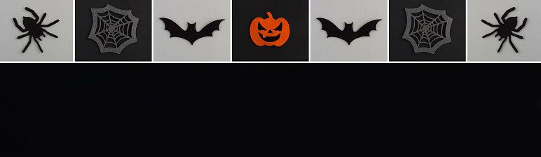Banner for Halloween. Decorative spiders, pumpkins, spider web and bat on the black and gray background. Copy space. Top view.
