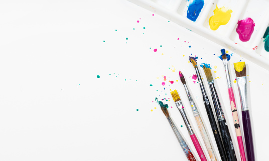 Art Paint brushes and palette with colorful paint splatter on white canvas paper. Copy space