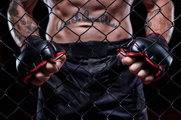 Dramatic image of a mixed martial arts fighter standing in an octagon cage. Powerful abdominal muscles. The concept of sports, boxing, martial arts. stock photo
