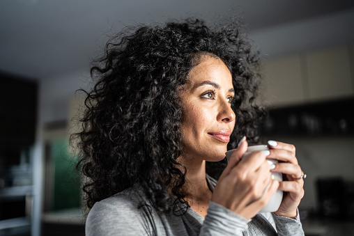 Mid adult woman looking away holding coffee mug in the kitchen at home