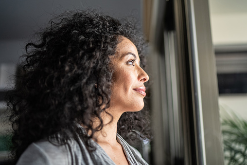 Mid adult woman looking through window at home