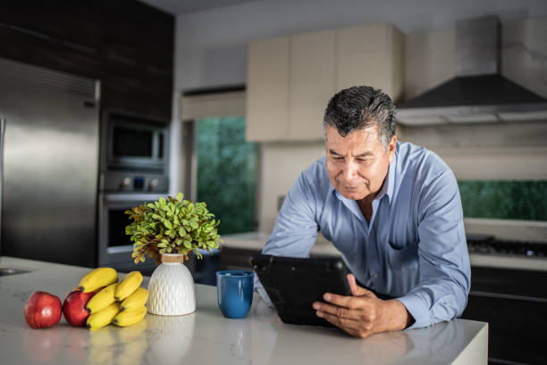 зрелый мужчина использует цифровой планшет на кухне дома - mexico only men senior men mature men стоковые фото и изображения