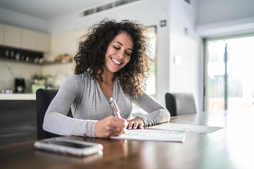 istock Mid adult woman filling document at home 1412934176