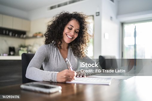 istock Mid adult woman filling document at home 1412934176