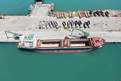 Aerial view of a large cargo ship unloading grain. Top view of a large cargo ship loading or unloading grain. Sea transportation. Truck carrying grain