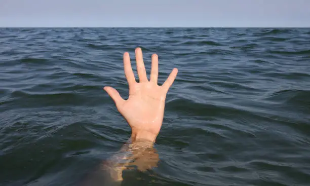 Photo of large open hand with five fingers emerging from the surface of the sea of a person about to drown under water