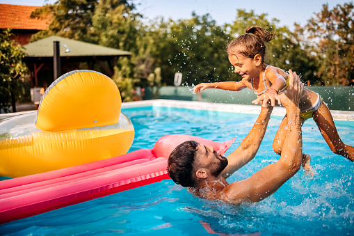 Father and daughter playing whilst swimming in a pool