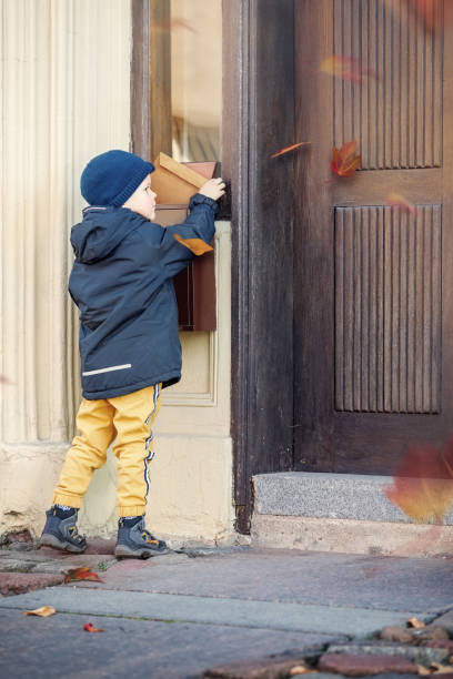istock Little boy with an envelope at post office. Child sending letter. Kid throwing card into a mail box. Postal service in Europe. Delivery and shipment at outdoor mailbox. 1412952829