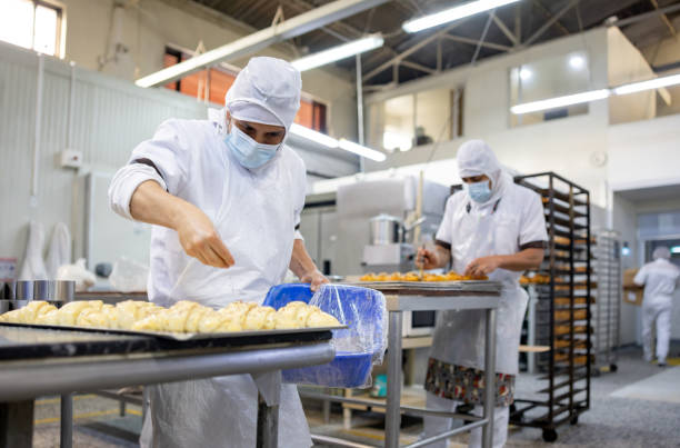 istock Baker working at an industrial bakery and sprinkling sesame seeds on a croissant 1412956728
