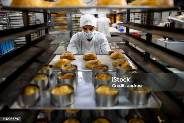 Woman Moving A Tray Of Pastries While Working At The Bakery Stock Photo - Download Image Now