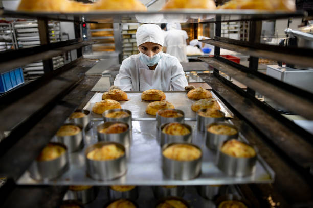 woman moving a tray of pastries while working at the bakery - buns of steel imagens e fotografias de stock