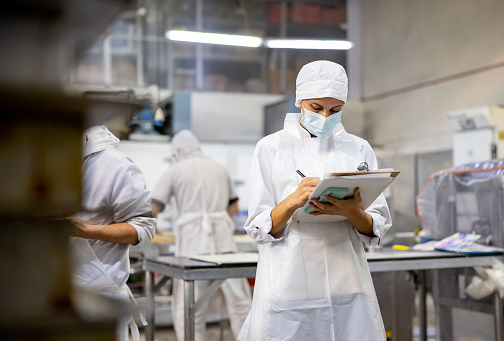 Portrait of a Latin American woman working at an industrial bakery and doing quality control and writing on a clipboard