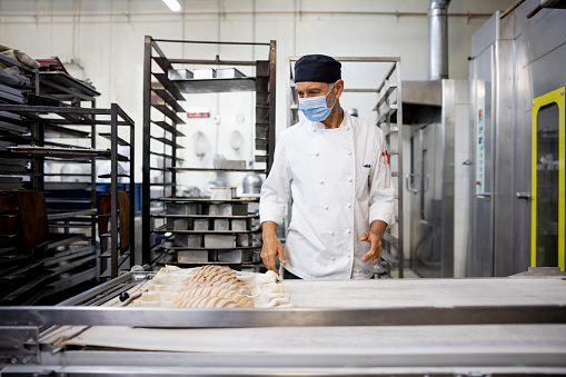 Latin American baker baking bread at an industrial bakery - manufacturing concepts