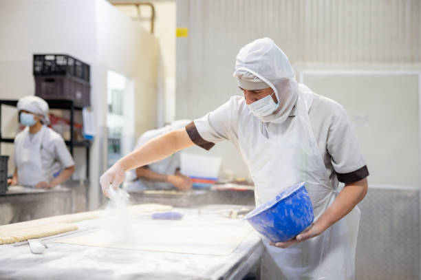 istock Baker working at an industrial bakery and sprinkling flour the dough 1412956779