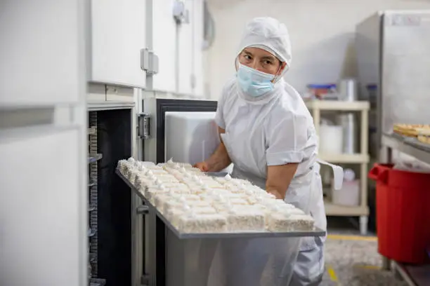 Latin American baker working at an industrial pastry shop and carrying a tray of mille feuille