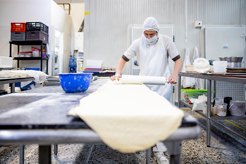 Latin American baker kneading the dough with a rolling pin at an industrial bakery