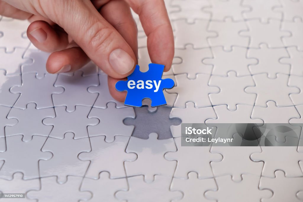 "EASY" Concept Woman hand holding last jigsaw piece of jigsaw puzzle. Horizontal composition with copy space. Easy concept. Effortless Stock Photo