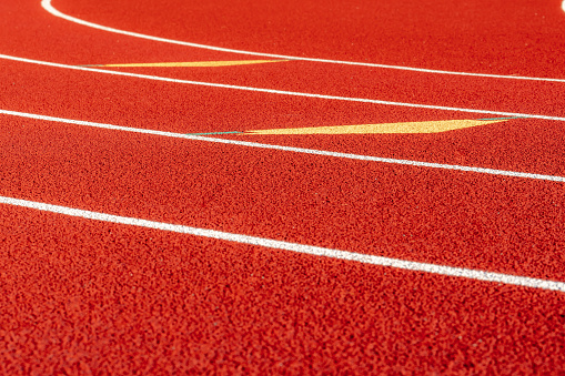 Inspiring close up of the start of an exchange zone on a new red running track with white lane lines and other markings.