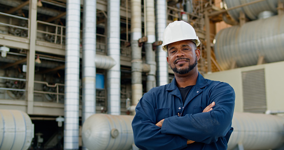 Portrait of a middle aged Black man wearing coveralls and a hard hat standing in front of a natural gas fired power station.