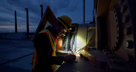 An electrician holds a flashlight to look into a generator at a power plant at night.