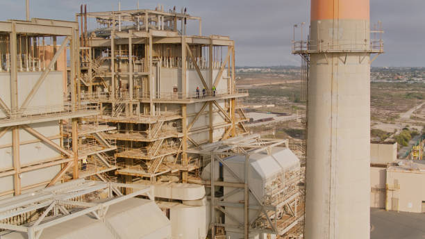 istock Drone Shot Looking Past Power Plant Smoke Stack Towards Workers on Elevated Walkway 1412965363