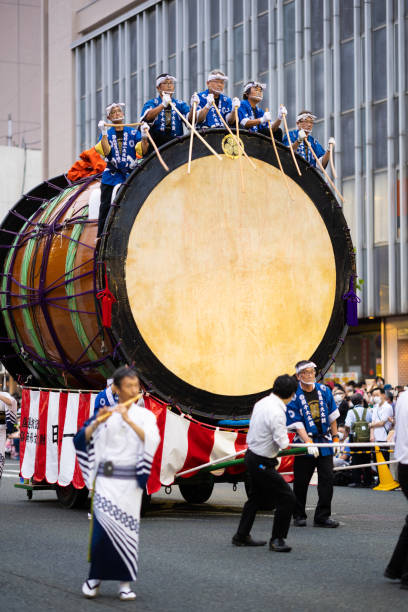 04 August 2022, Morioka, JP. Sansa Festival. Japan's biggest Taiko drum being pulled down a city street while several men play while sitting on it.