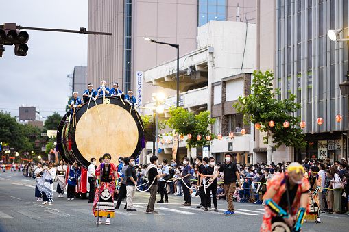 04 August 2022, Morioka, JP. Sansa Festival. Japan's biggest Taiko drum being pulled down a city street while several men play while sitting on it.
