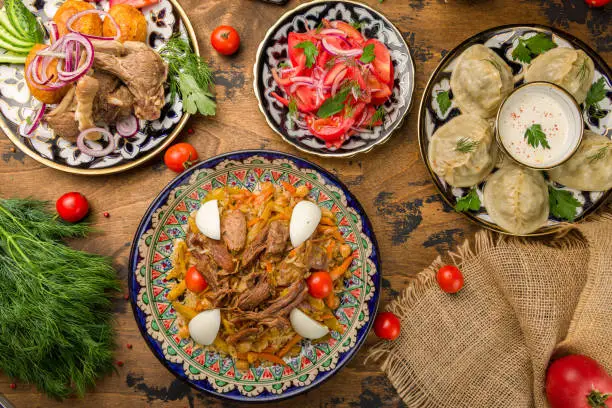 Photo of Pilaf festivities with beef, manti with beef,kazan kebab with lamb, salad tomatoes with red onion achik chuchuk top view on wooden table