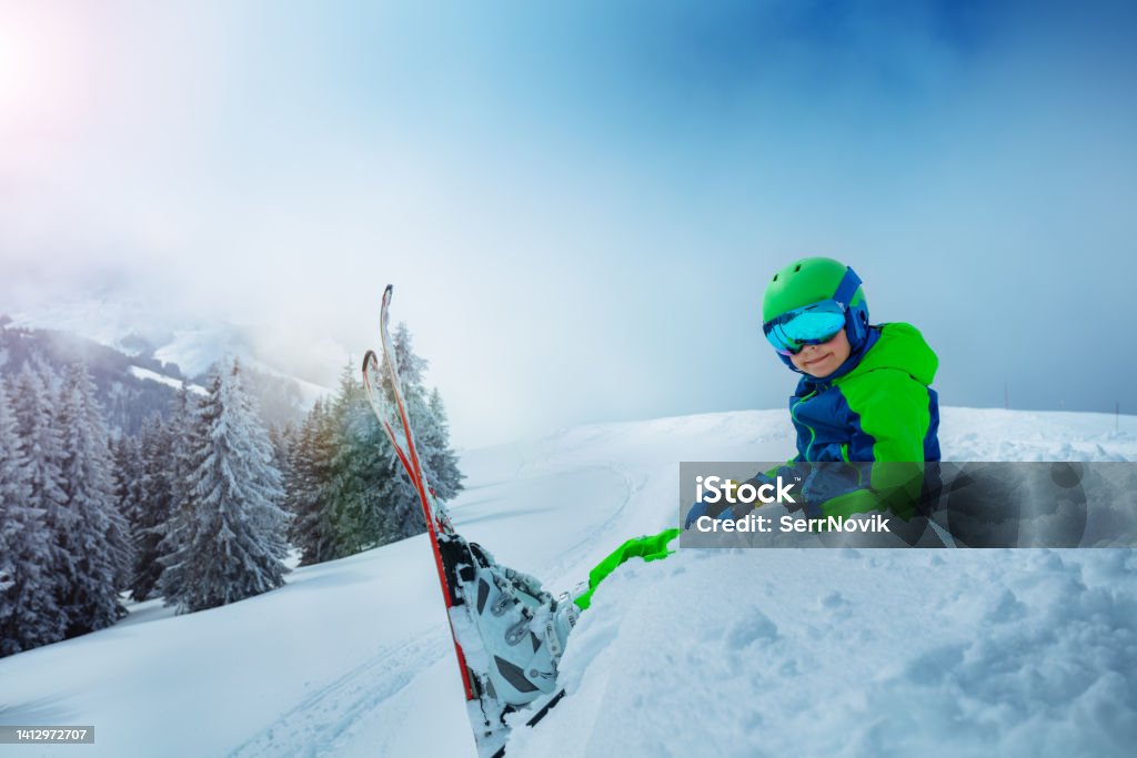 Side view of the boy with mountain ski sit in snow Side view of the boy with mountain ski sit in the snow over snowy forest after strong storm 10-11 Years Stock Photo