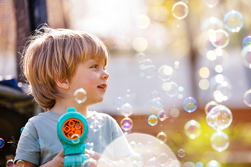 Close portrait of a cute boy play with soap bubbles holding bubble gun it the playground