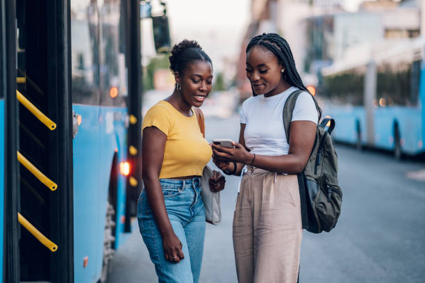 Two african american woman waiting for a bus and using a smartphone stock photo