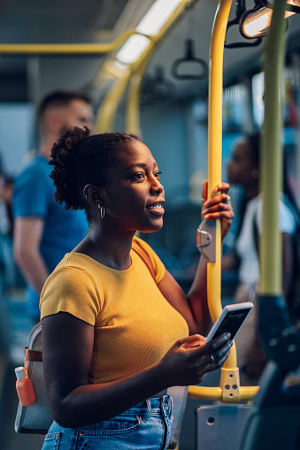 Young african american woman reading a text message on her smartphone while riding a bus in the night. Black woman catching up on social media while in a bus during her morning commute.