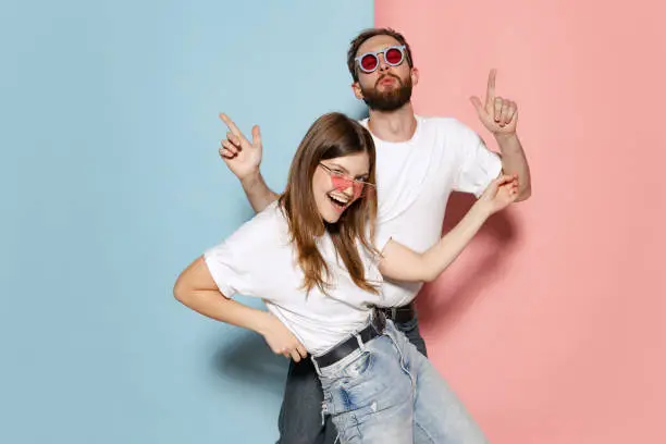 Photo of Young stylish happy man and excited girl dancing hip-hop at studio on blue and pink trendy color background. Emotions, youth, love and active lifestyle concept