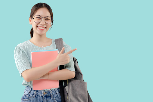 Asian student glasses girl over isolated mint green background pointing finger to the side with copy space.