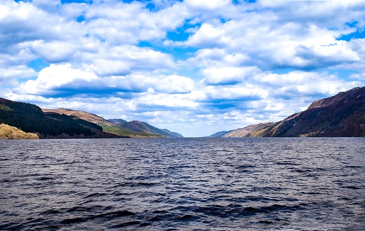 Beautiful Loch Ness, lake in the Scottish Highlands, Scotland, with mountains surrounding, vibrant blue sky with clouds above. Home of the mythical Loch Ness monster.