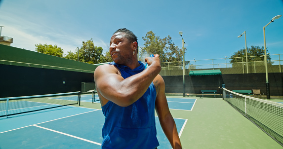 A young Cape Verdean man sprays on sunscreen on a pickleball court