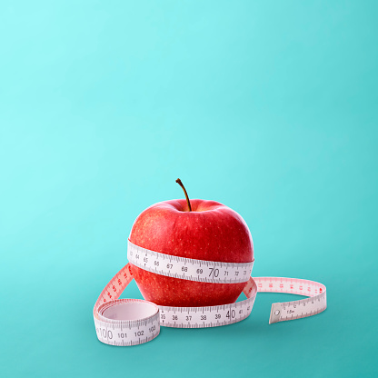 Red apple tied up measurement tape on light blue background with copy space.
Diet concepts.